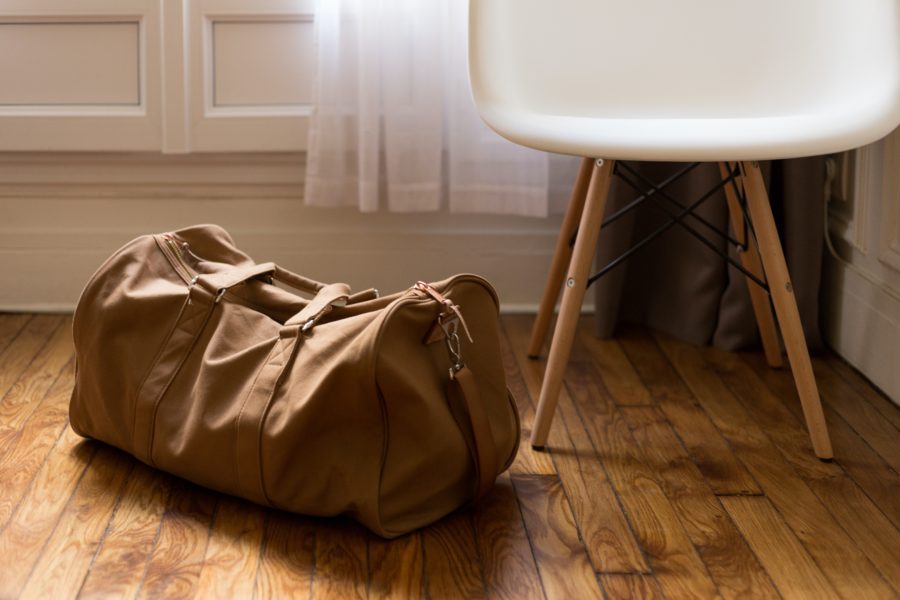 A brown duffel bag on the floor beside a white chair