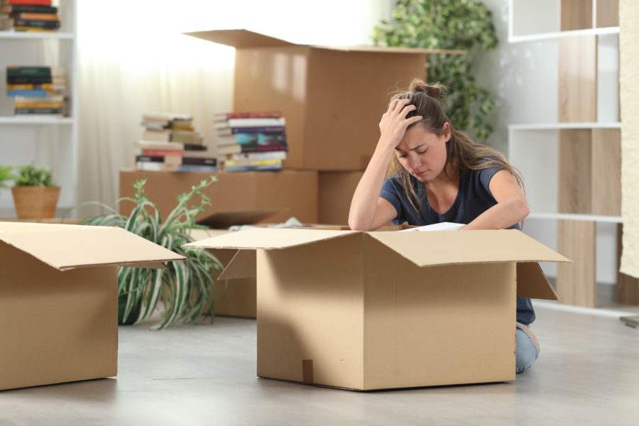 A girl relocating to another place holding her head while being surrounded by boxes